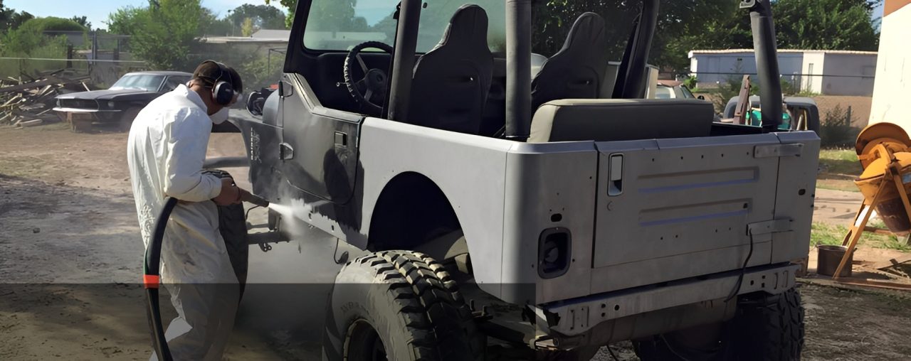 Man sandblasting a vehicle outdoors